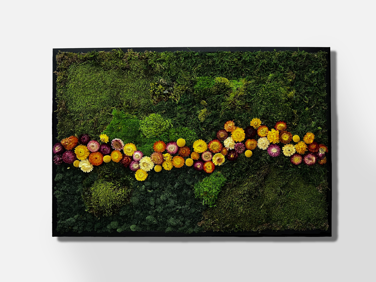 Large moss wall art of varying shades of green with a horizontal river of yellow, pink, and dark purple flowers in the middle